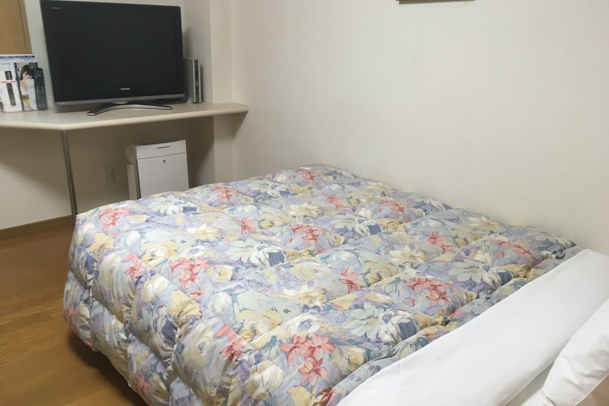 Ein Schlafzimmer mit einem blumigen Bettüberwurf, einem Fernseher auf einem Standfuß und einem kleinen weißen Schrank.