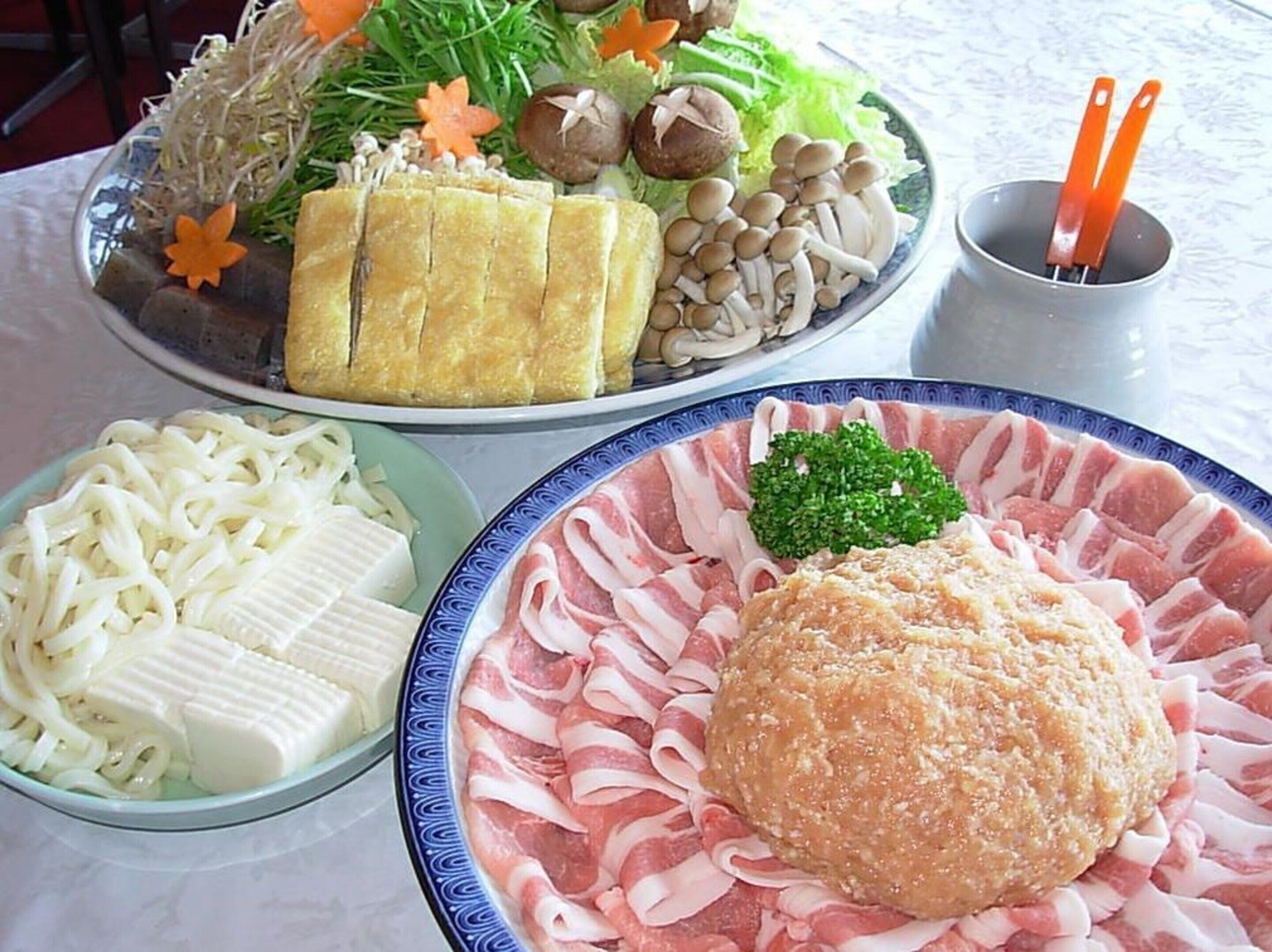 A table with various dishes including noodles, sliced meat, and vegetables.