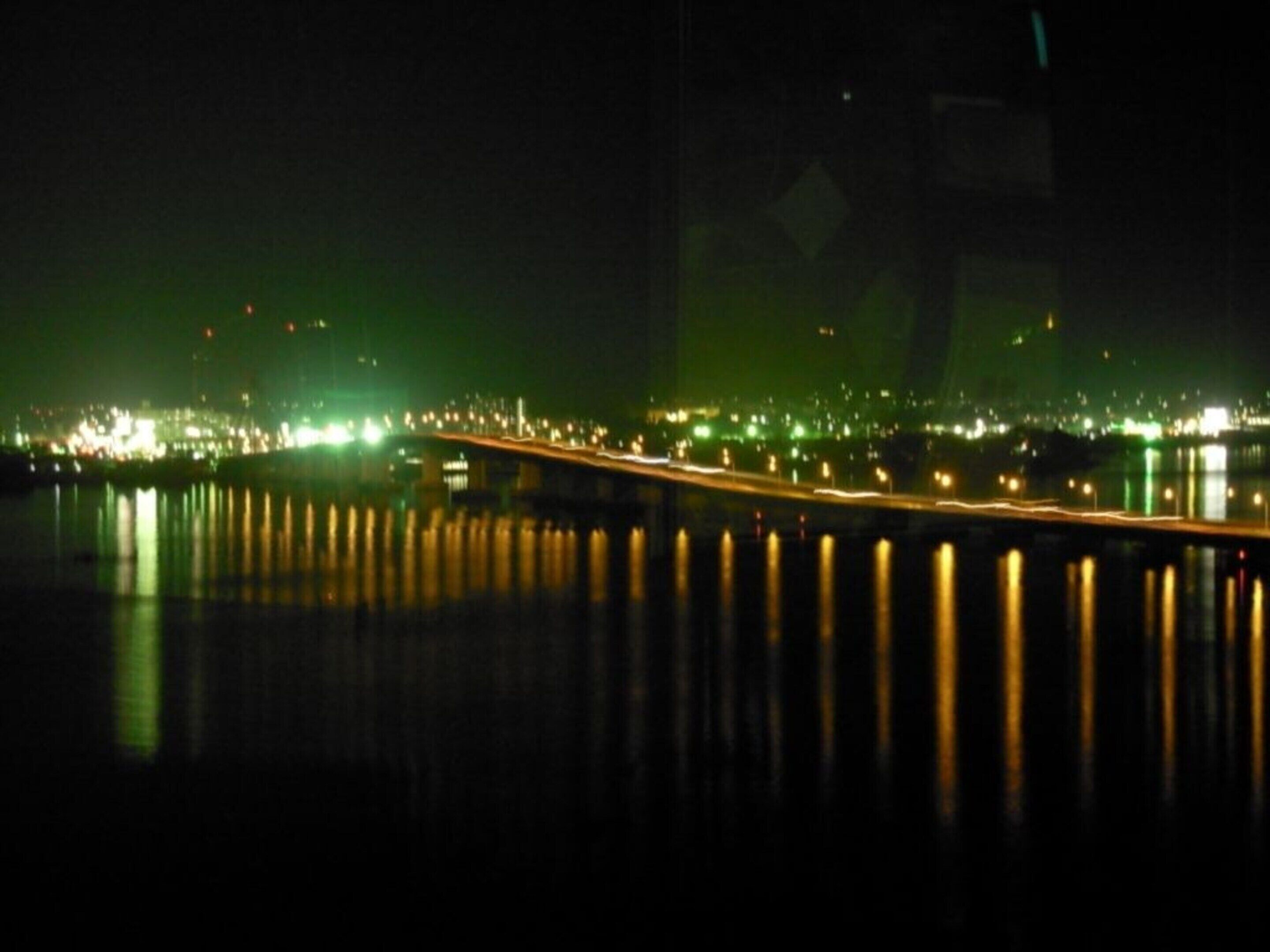 Ein nächtlicher Blick auf eine Brücke, deren Lichter sich im Wasser spiegeln.