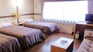 Une chambre d’hôtel avec deux lits, un bureau, une chaise, une lampe et une fenêtre avec des rideaux.
