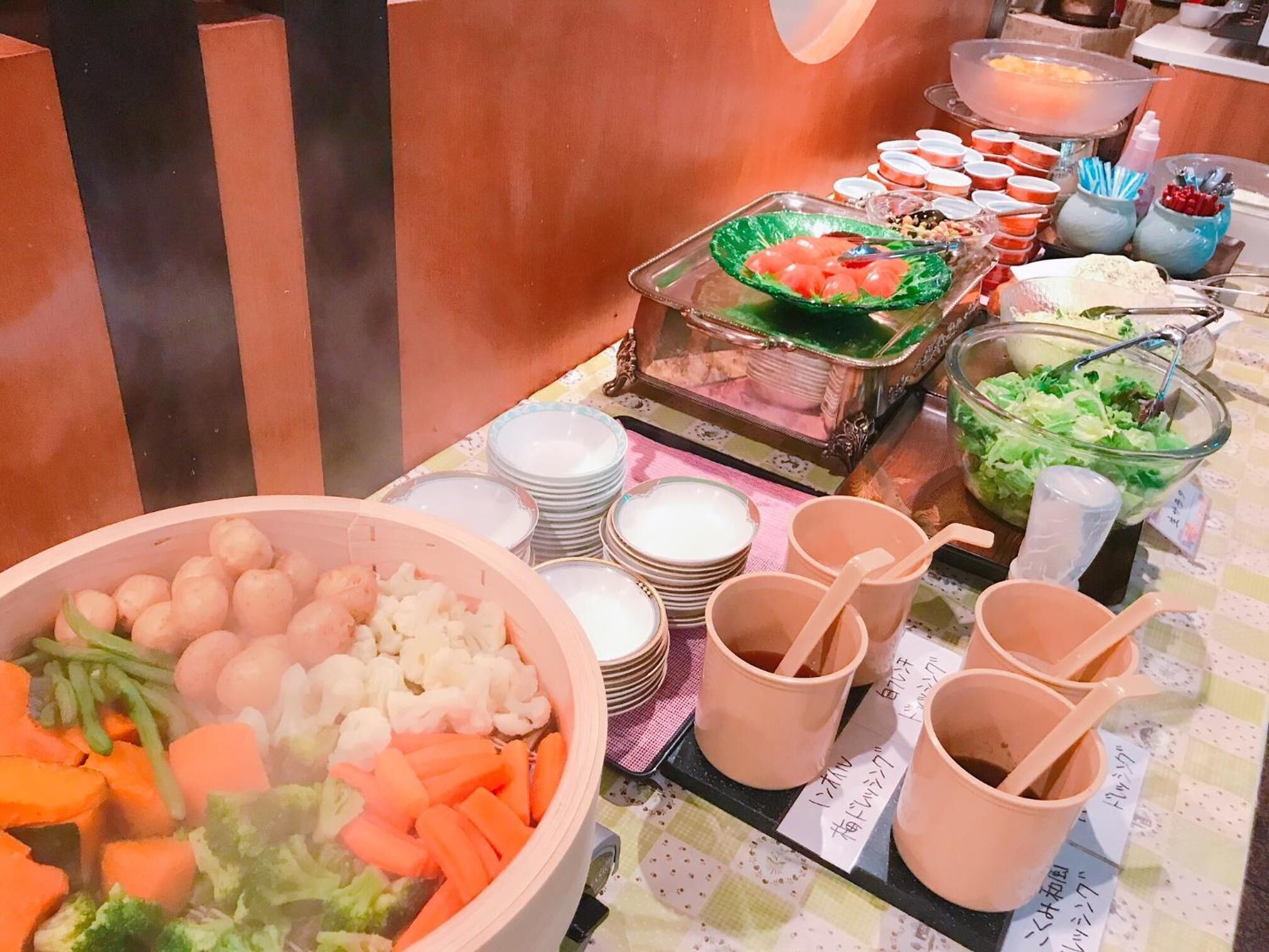 A buffet table with various dishes, including a large bowl of vegetables, several plates, and cups.