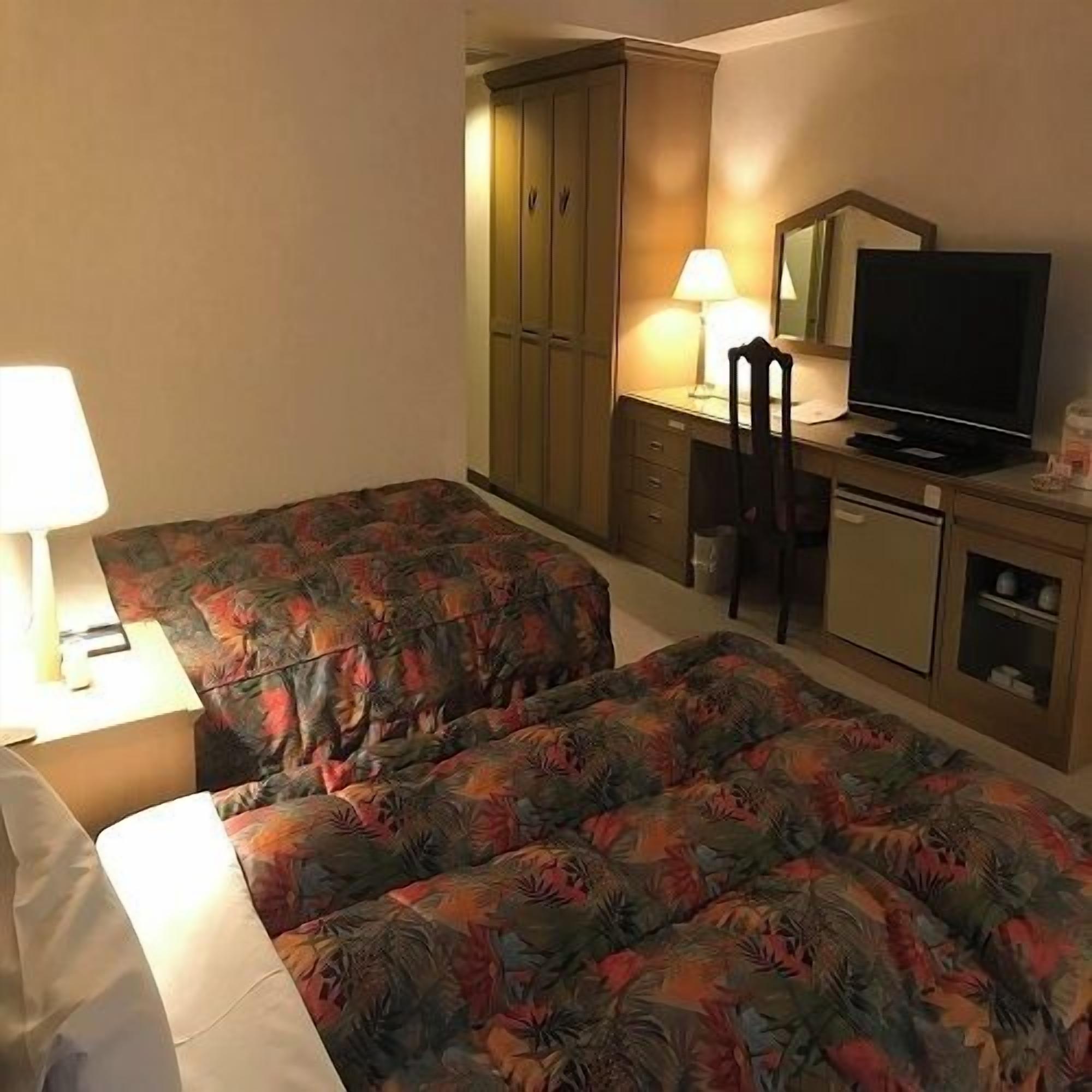 A hotel room with two beds, a desk with a chair, a television, and a cabinet.