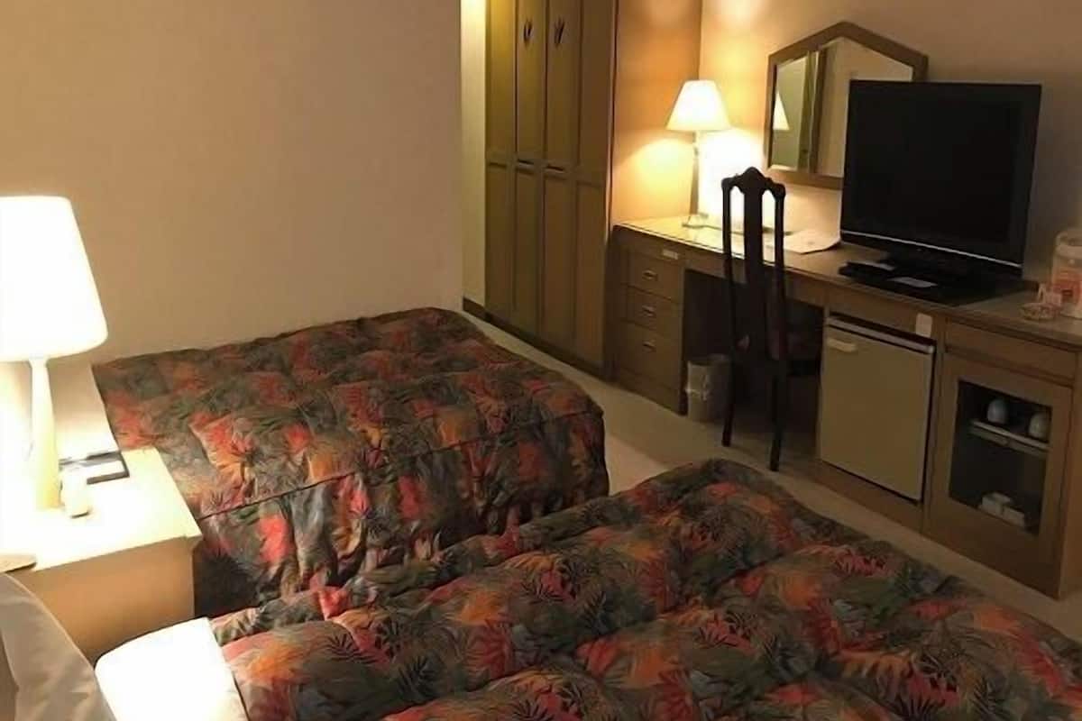 A hotel room with two beds, a desk with a chair, a television, and a cabinet.