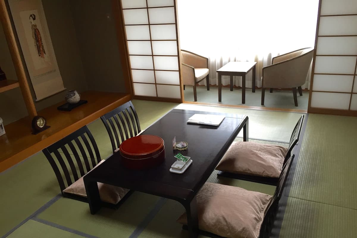 A traditional tatami mat room with a low table, chairs, and a futon bed.