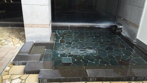 Un suelo de baldosas mojado con un borde de piedra y escalones que conducen a una puerta.
