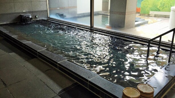 Piscina interior rectangular con agua cristalina, rodeada de baldosas de piedra y una barrera de vidrio.