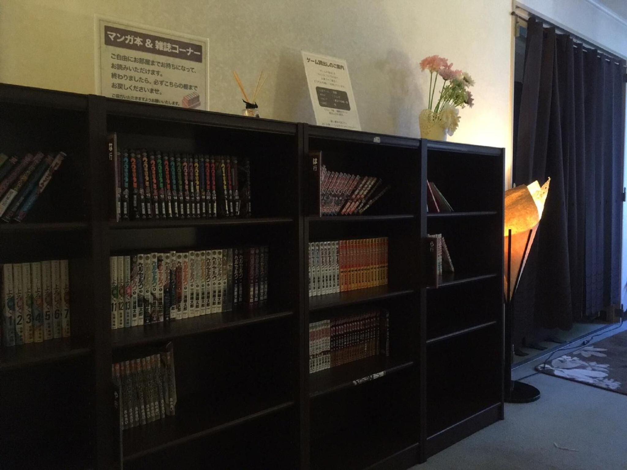 A bookshelf filled with books, a vase with flowers, and a lamp.