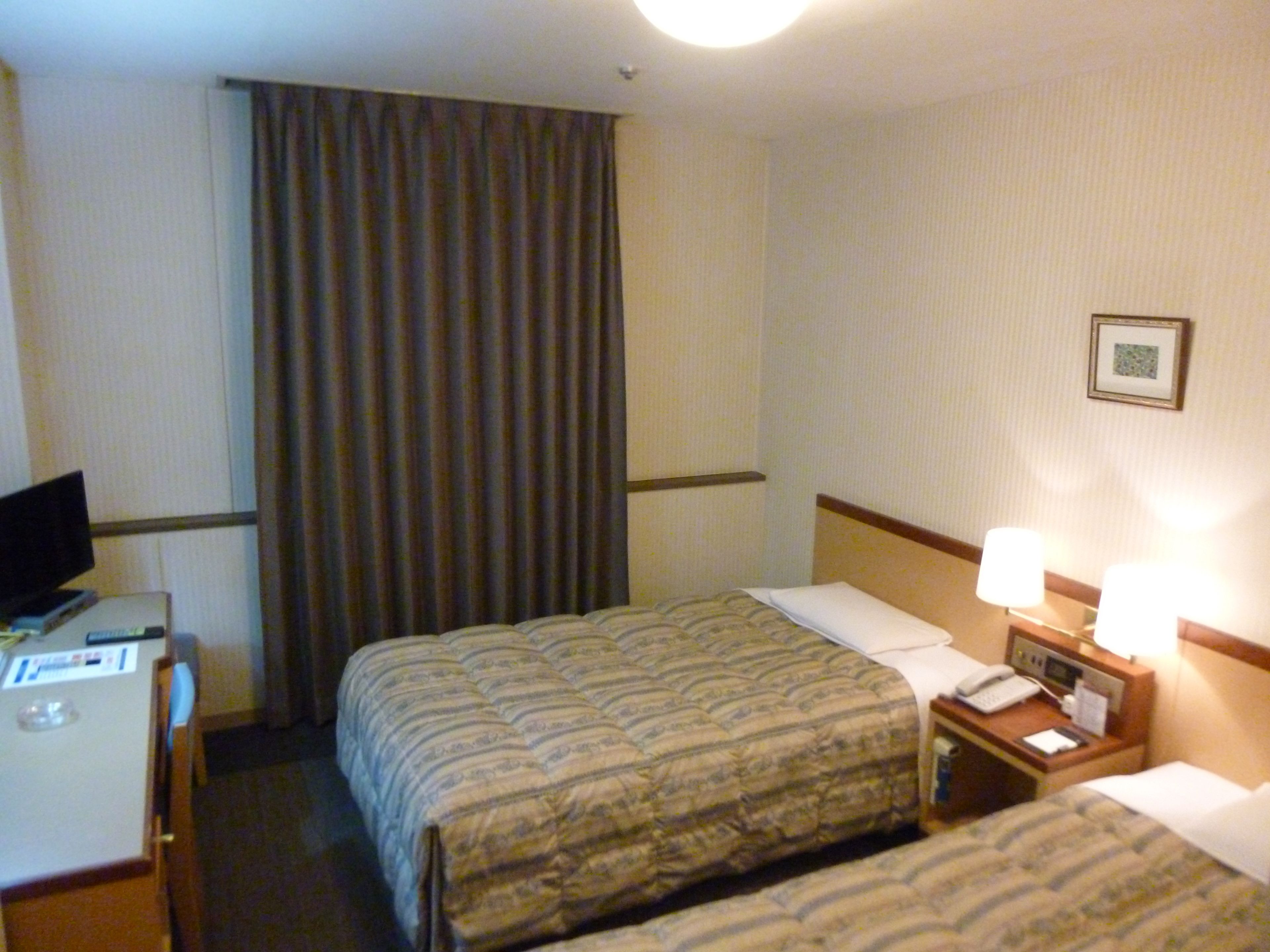 A hotel room with two beds, a desk with a computer, a telephone, and a nightstand with lamps.