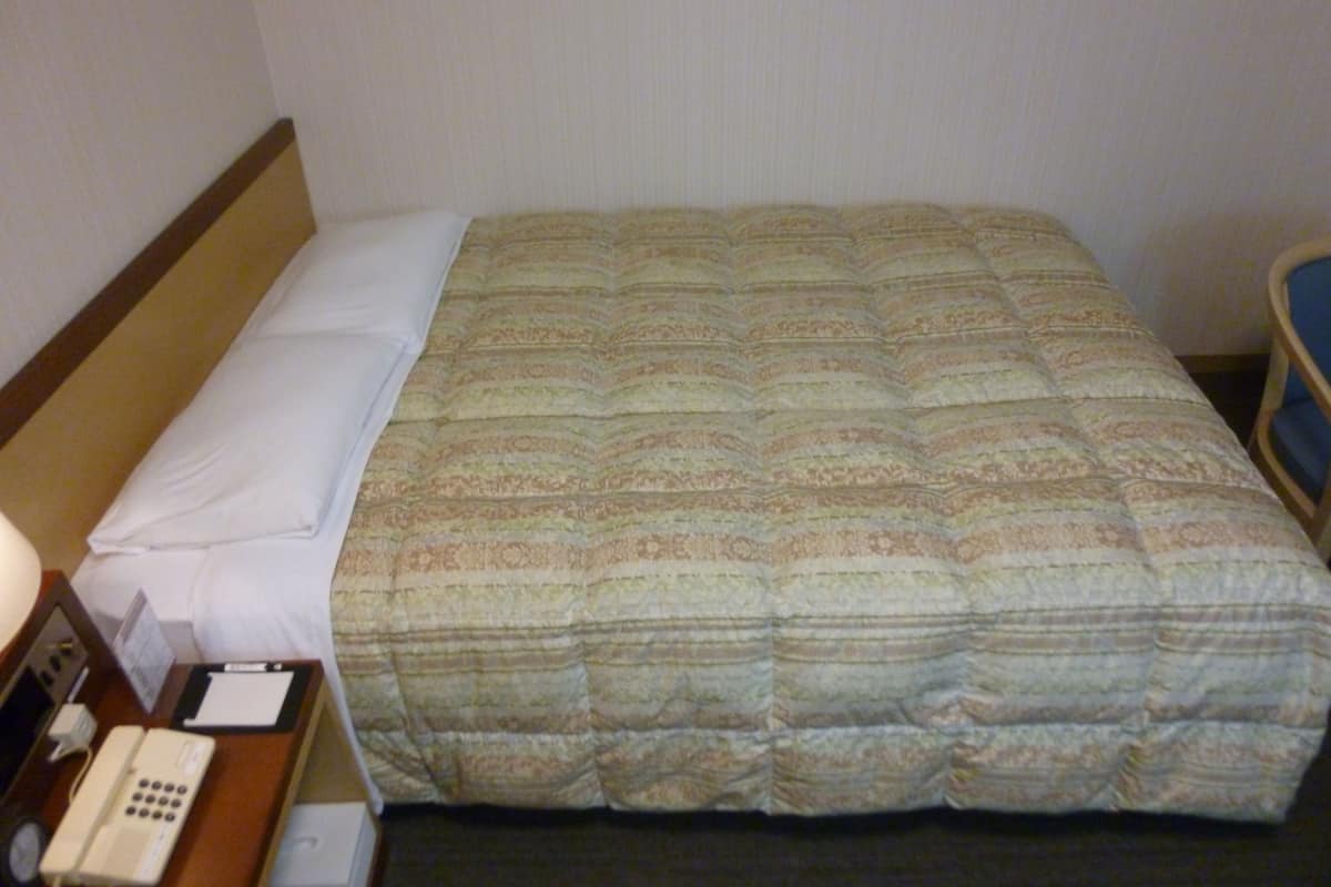Een hotelkamer met een bed, een nachtkastje met een telefoon en een stoel.