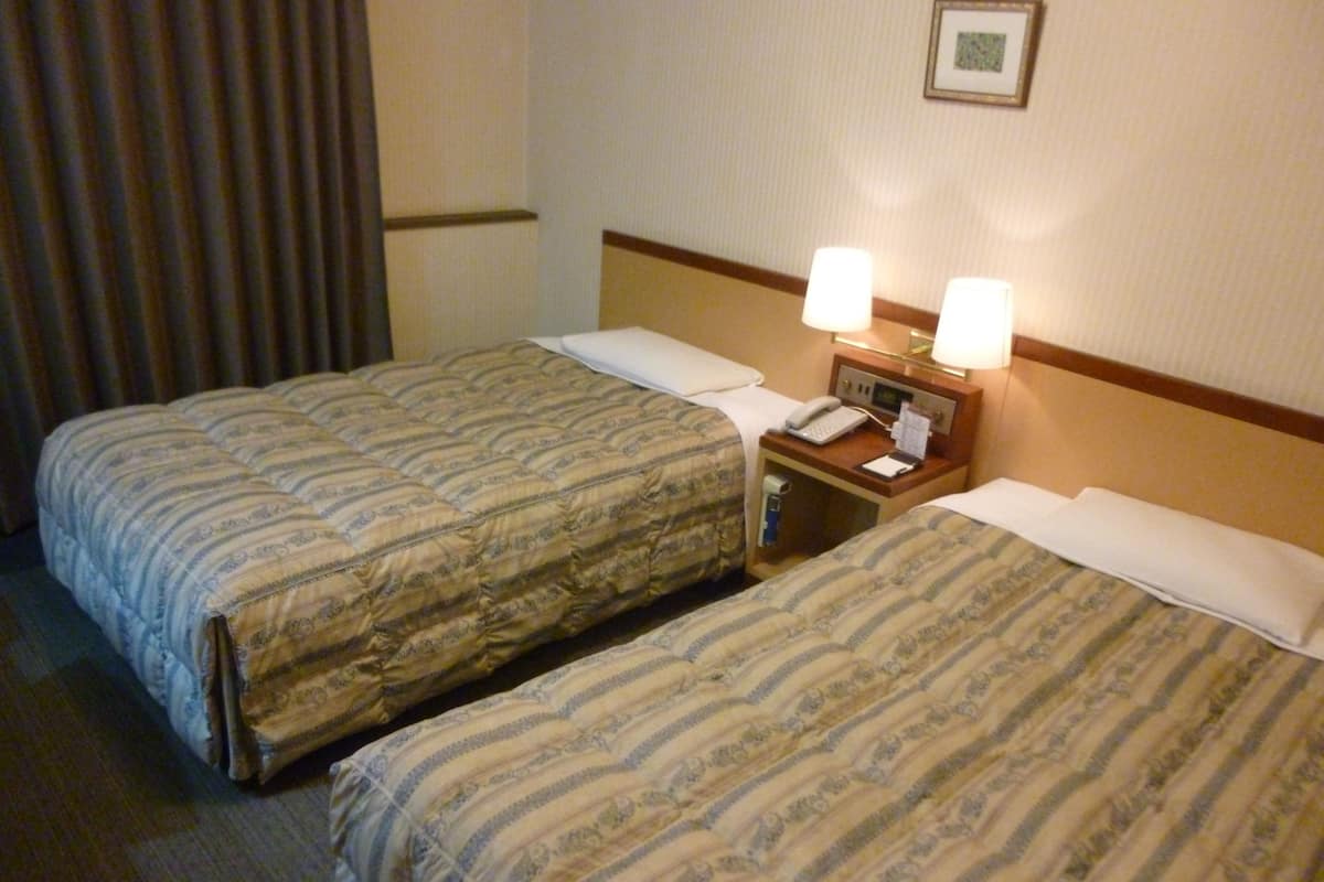 Een hotelkamer met twee bedden, elk voorzien van een beddegoed met een patroon, een nachtkastje met een lamp en een ingelijst schilderij aan de muur.