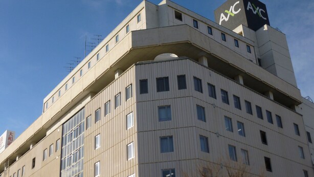 Un immeuble à plusieurs étages, sur lequel on peut voir un grand panneau « AXC » au sommet.