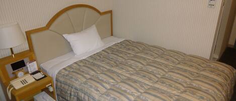 A hotel room with a bed, a nightstand with a lamp, a telephone, and a small table with a tissue box.