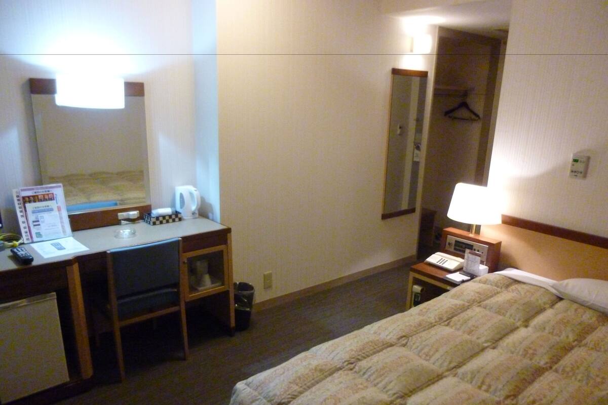 Een hotelkamer met een bed, een bureau met stoel, een telefoon en een spiegel.