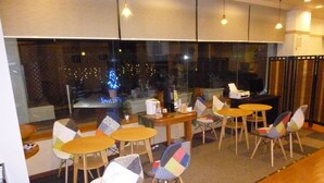 Un espace de restauration moderne avec des tables rondes et des chaises colorées, de grandes fenêtres offrant une vue sur les lumières de la ville, et une ambiance chaleureuse.