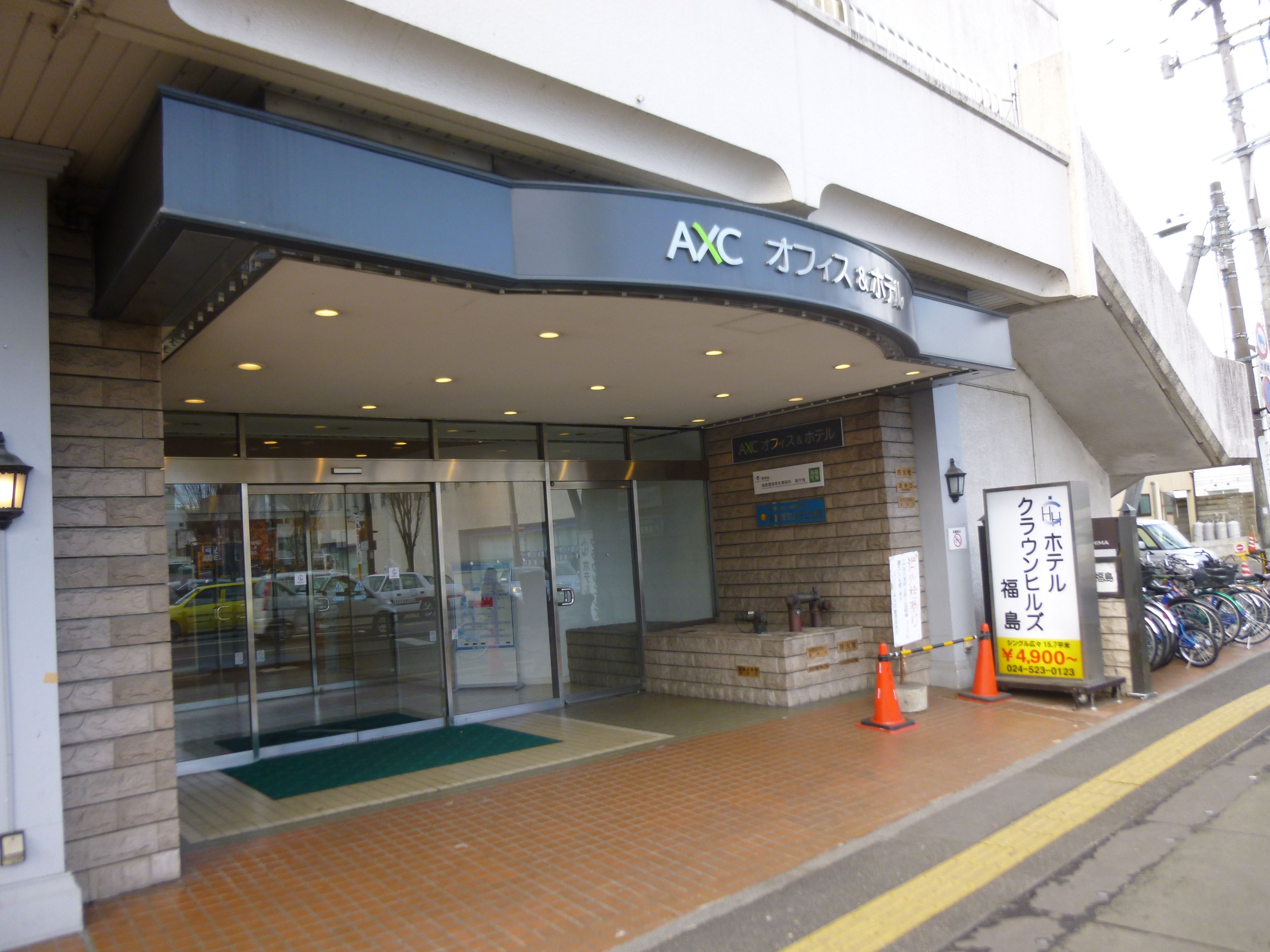A hotel entrance with a glass door, a signboard with Japanese text, and a bicycle parking area.