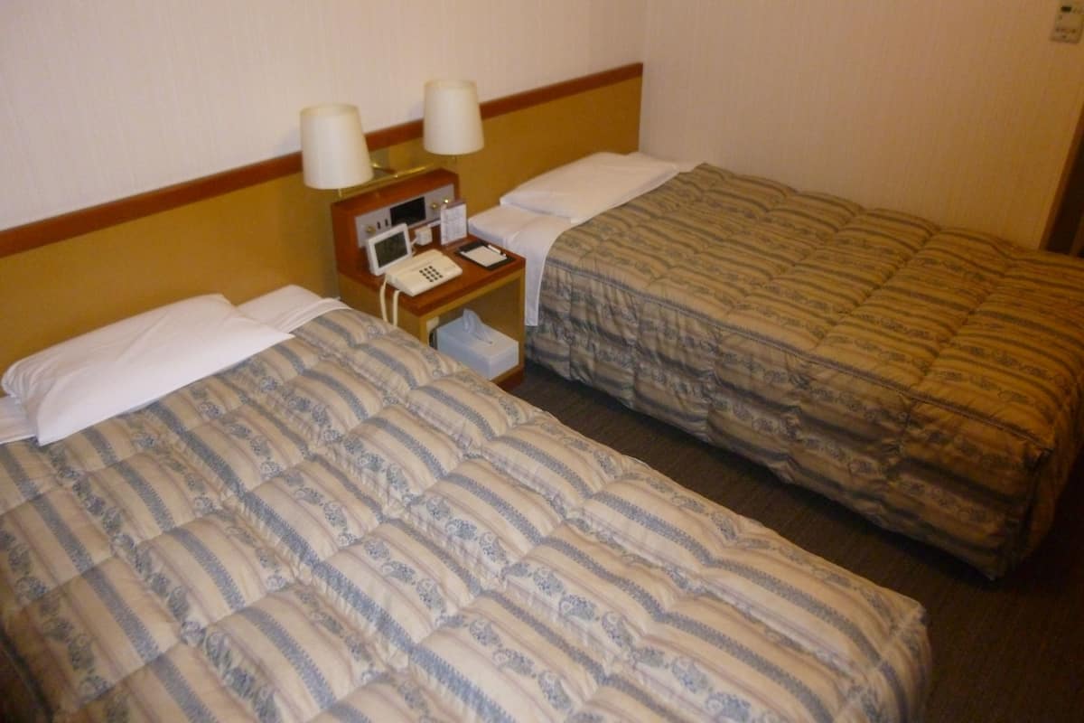 Twee enkele bedden met gestreepte beddengoed, een nachtkastje met een lamp, een telefoon en een klein prullenbakje.