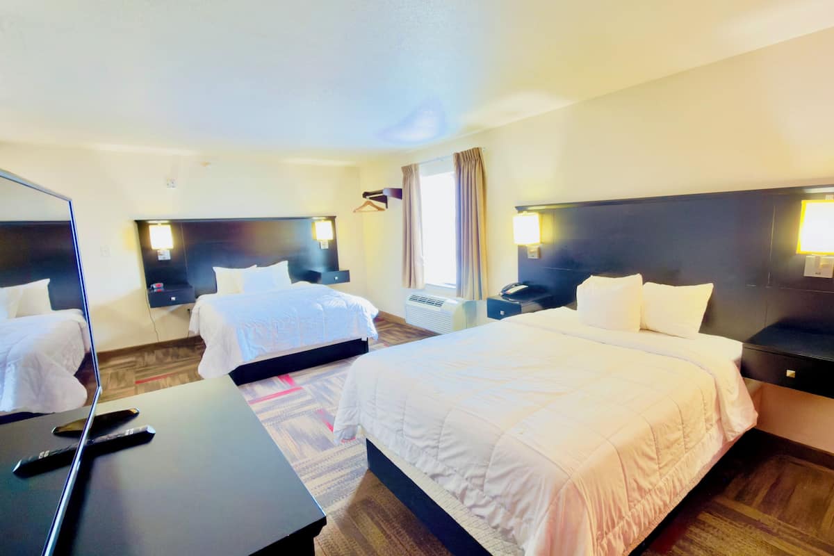 A hotel room with two beds, a desk, and a mirror.