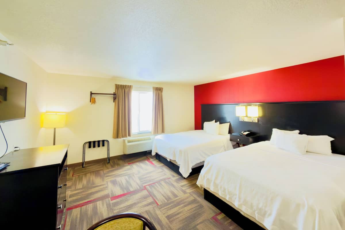 A hotel room with two beds, a desk, a chair, a TV, and a window with curtains.
