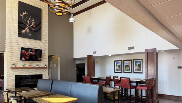 A modern hotel lobby with a fireplace, seating area, dining tables, and artwork on the walls. - Black Gold Suites Tioga (Tioga)