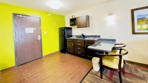 A compact kitchen with a refrigerator, microwave, and a small dining area with a table and chairs. - Black Gold Suites Tioga (Tioga)