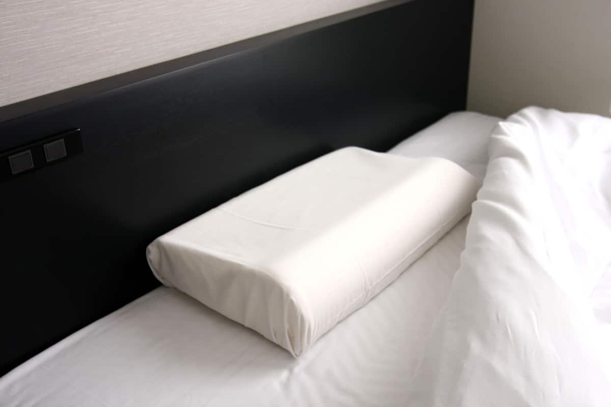 A neatly made bed with white linens and a black headboard.