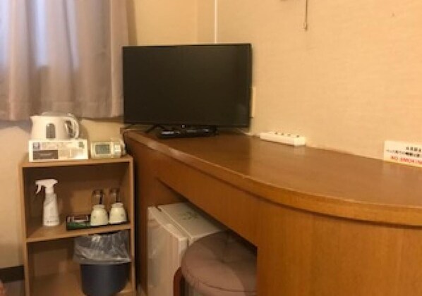 Habitación de hotel con televisor sobre un mueble de madera, un estante pequeño con artículos de aseo y un cubo de basura.