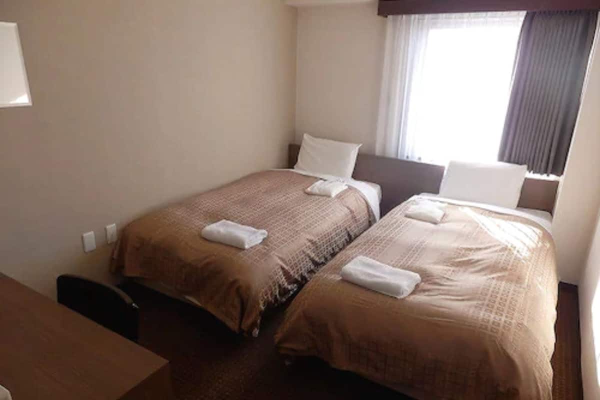 Ein Hotelzimmer mit zwei Einzelbetten, beide mit brauner Bettdecke und weißen Kissen. Im Zimmer befindet sich ein Holztisch und ein Stuhl.