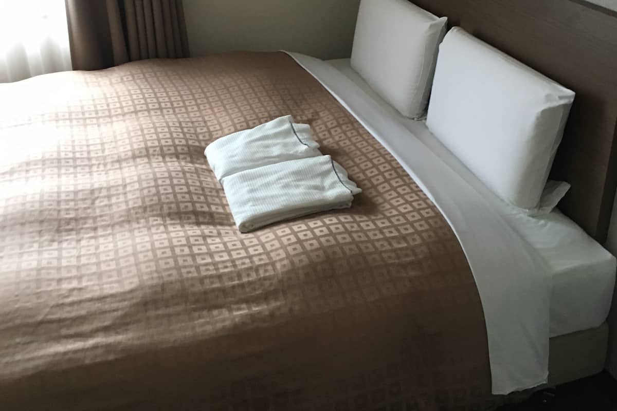 Ein Hotelzimmer mit einem aufgereihten Bett, einem Kopfteil und einem Fenster mit Vorhängen.