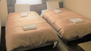 Ein Hotelzimmer mit zwei Betten, jeweils mit Kissen und einem Handtuch. Das Zimmer verfügt über ein Fenster mit Vorhängen, einen Teppichboden und schlichte Wände.