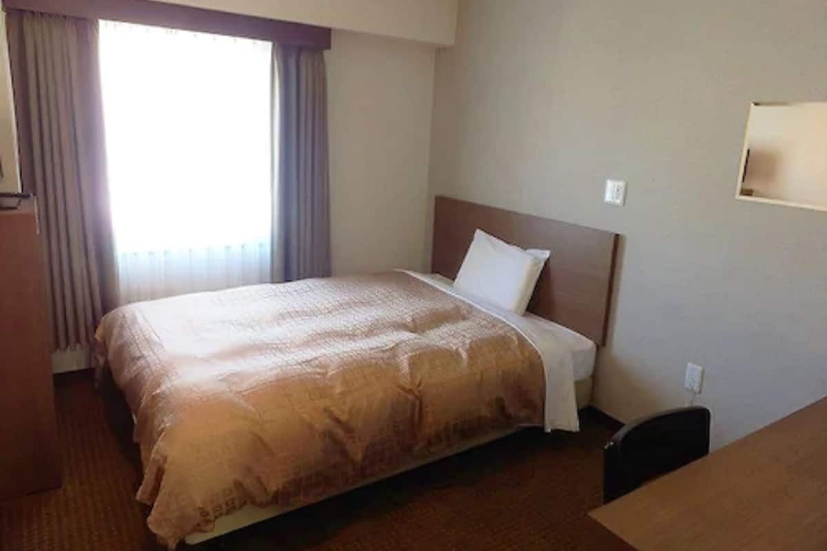 Ein Hotelzimmer mit Bett, Schreibtisch und einem Fenster mit Vorhängen.