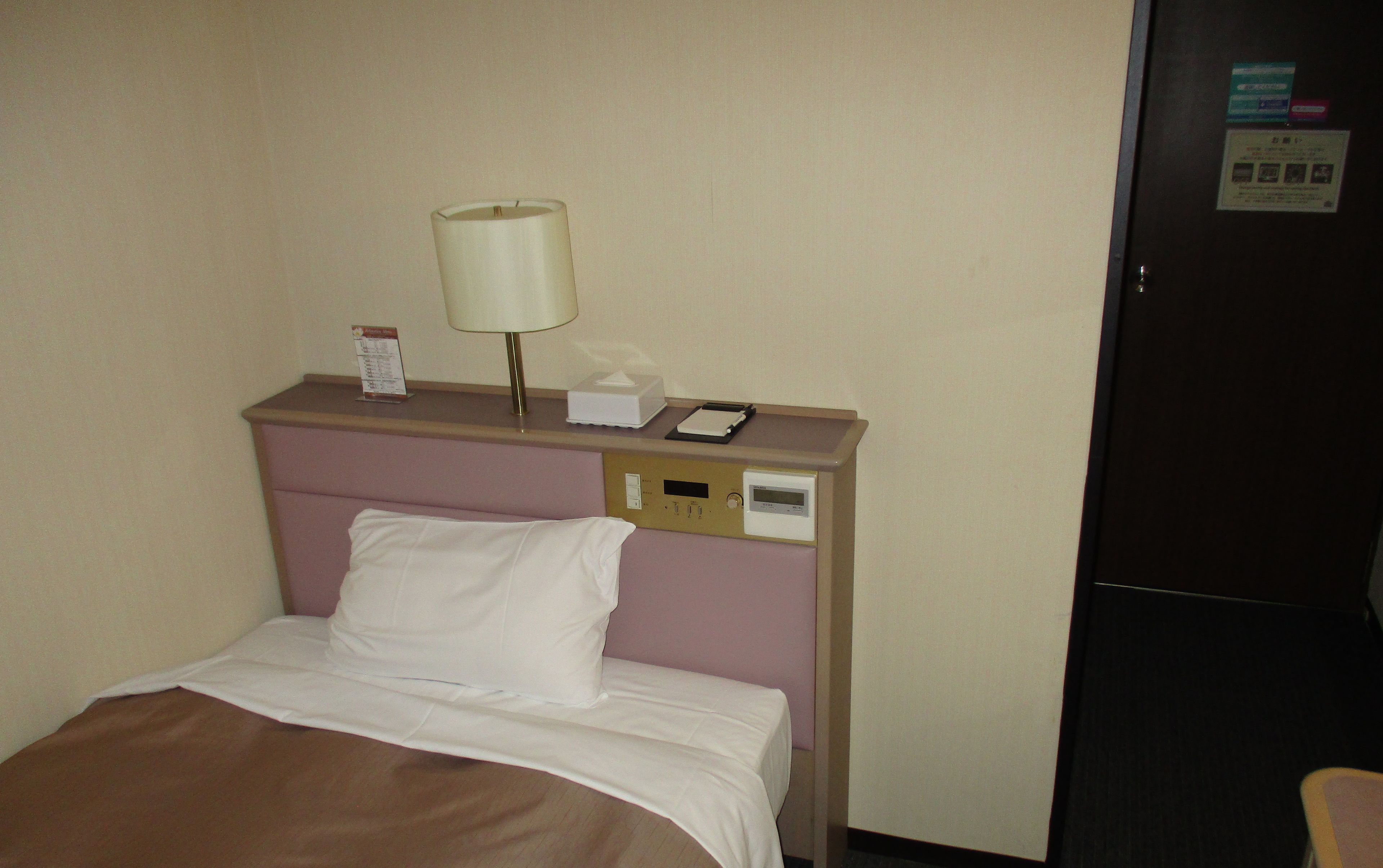 A hotel room with a bed, a bedside table with a lamp, a phone, and a refrigerator.
