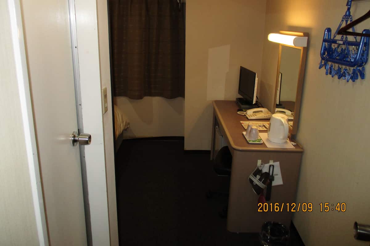 A hotel room with a bed, a desk with a computer, a telephone, and a lamp.