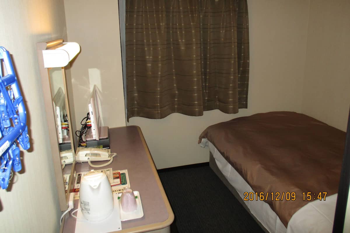 A hotel room with a bed, a desk with a telephone, a mirror, and a window with curtains.