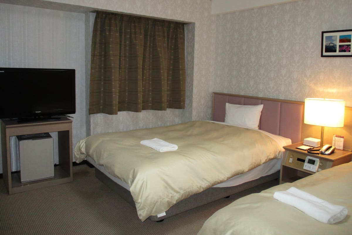 A hotel room with a bed, a television, a nightstand, and a lamp.