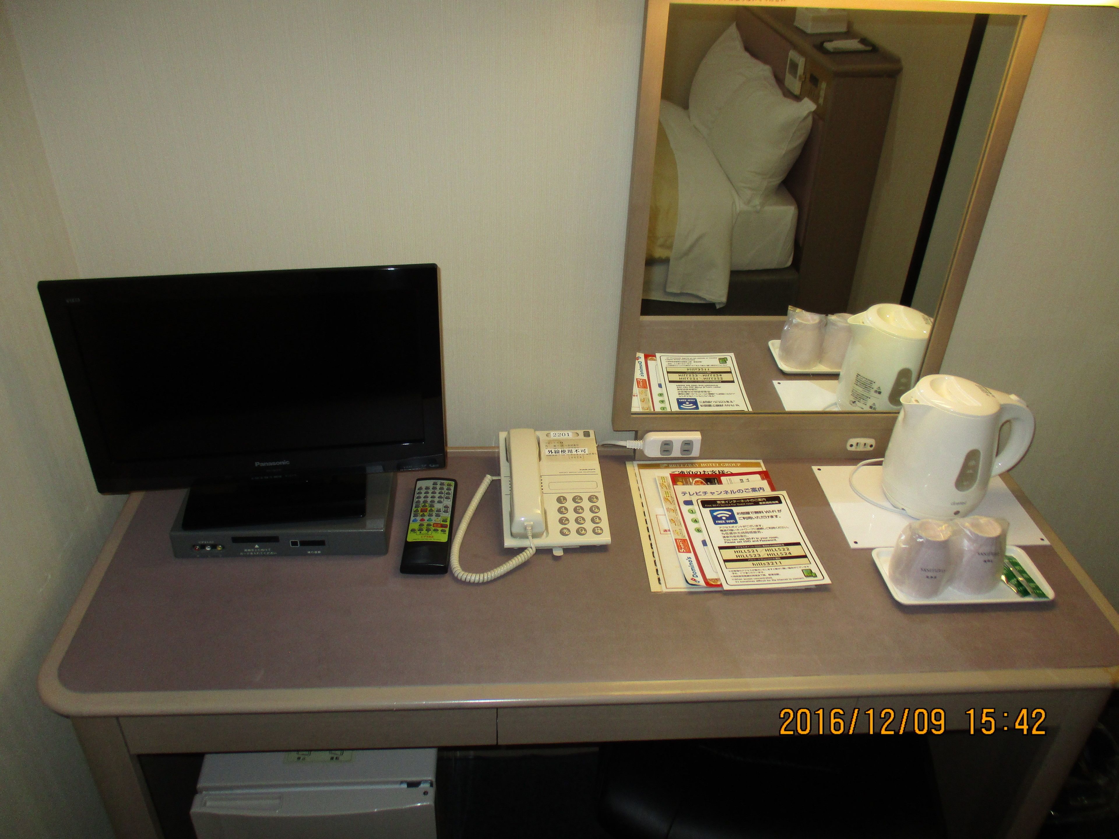 A hotel room with a television, telephone, remote control, a mirror, a coffee maker, and a small table with a menu.