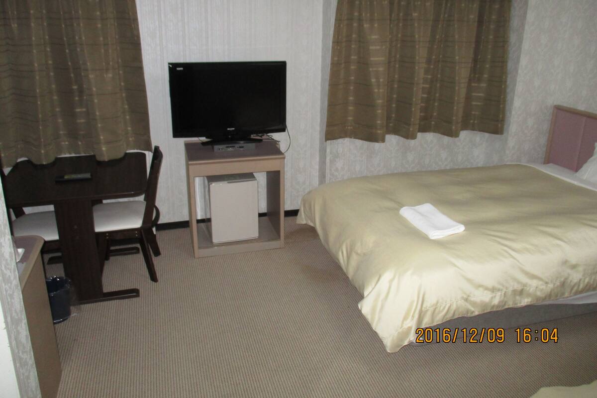 A hotel room with a bed, a desk with a television, and curtains.