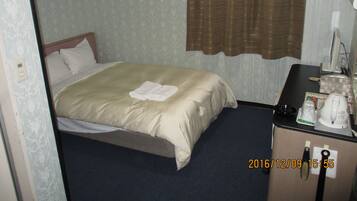 Una habitación de hotel con cama, escritorio con teléfono y ventana con cortinas.
