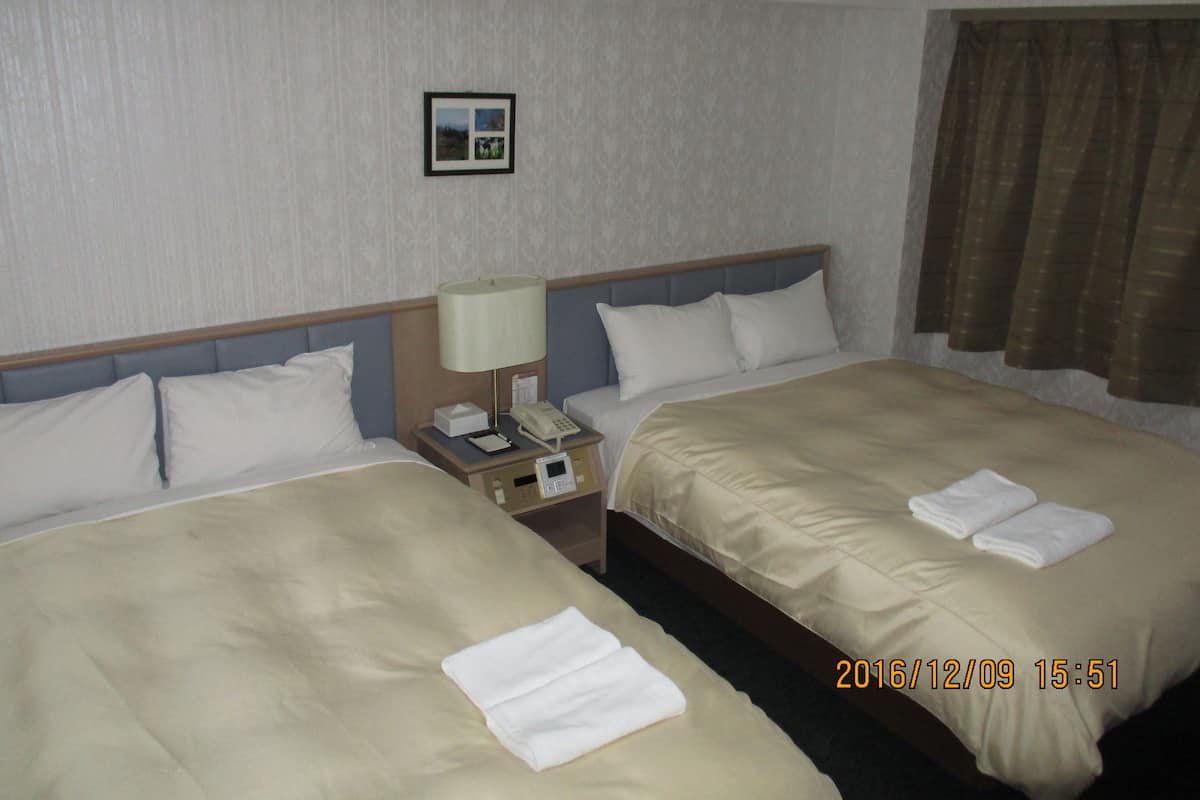 A hotel room with two beds, a nightstand with a lamp and phone, a picture on the wall, and a window with curtains.