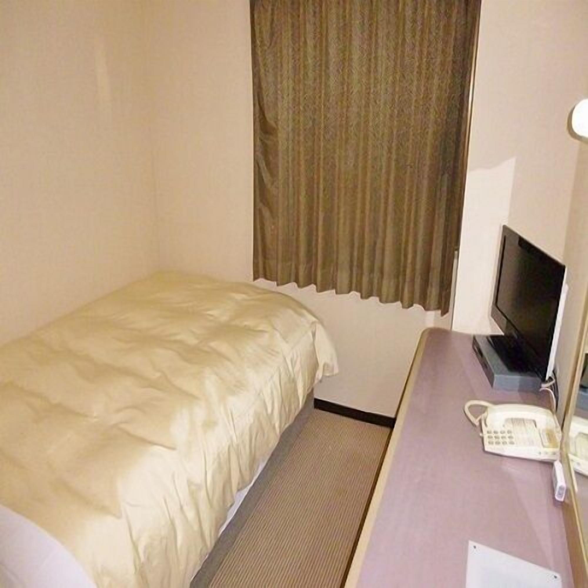 A small hotel room with a single bed, a desk with a telephone, and a television.