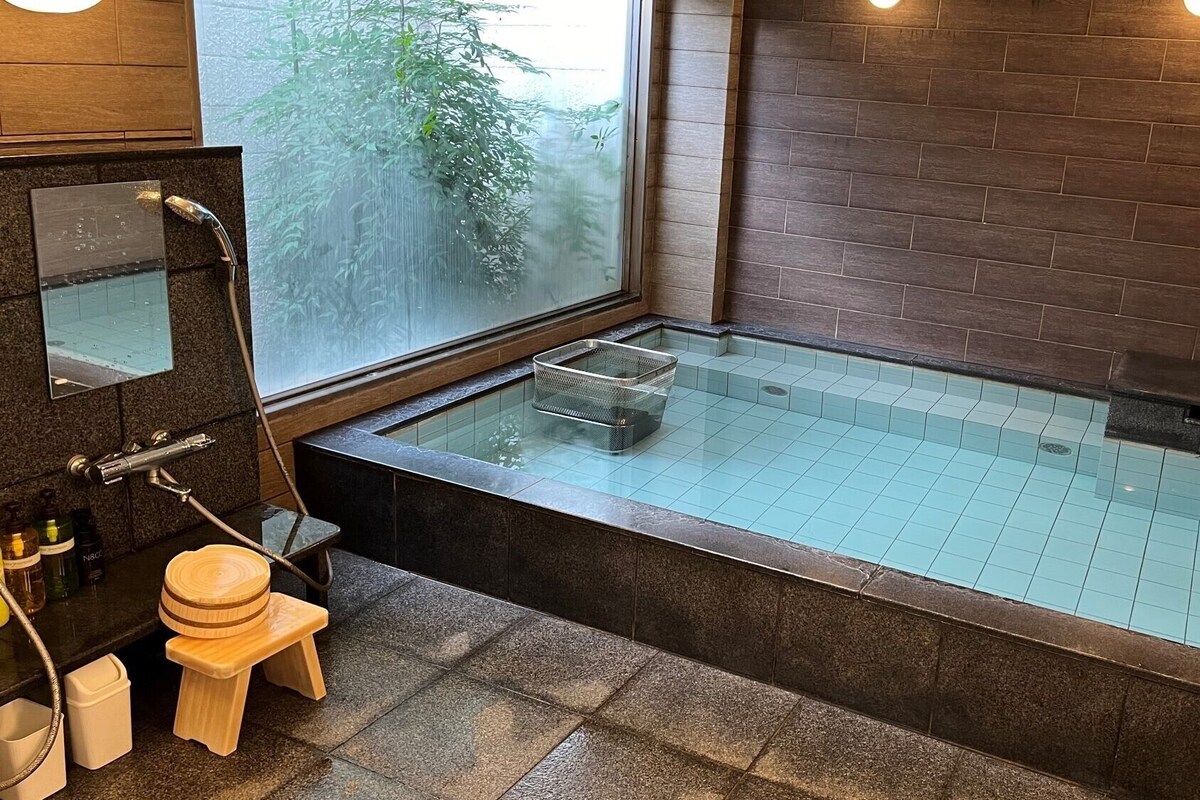 Un baño moderno con bañera de hidromasaje con mampara de vidrio, un taburete de madera y un espejo grande.