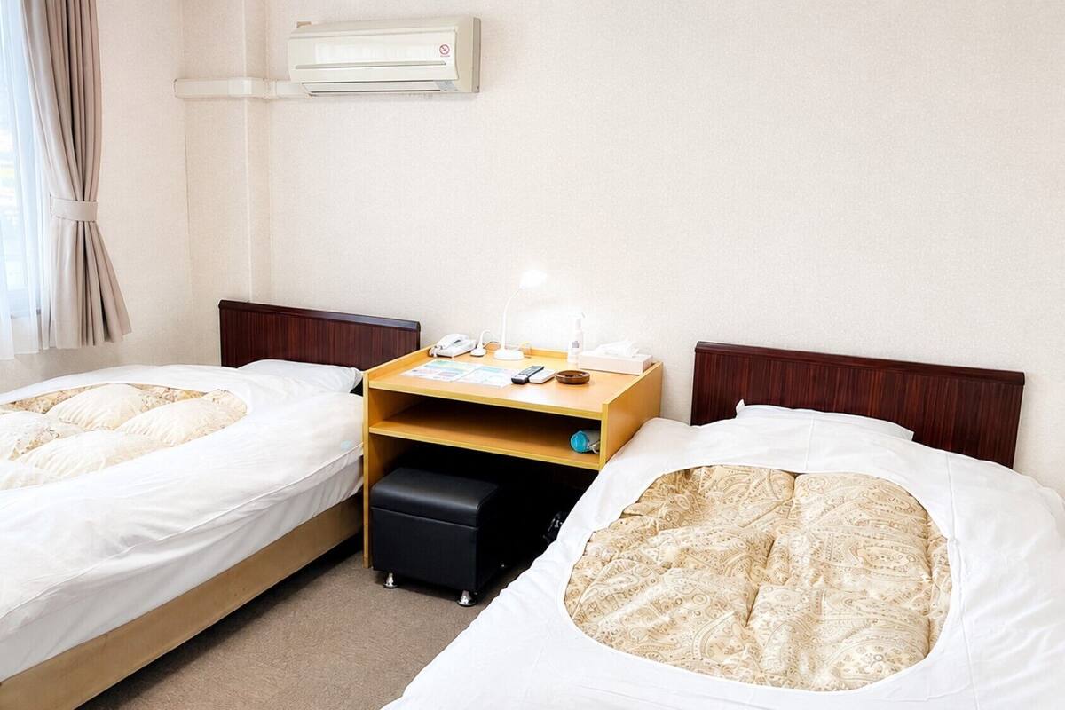 Une chambre d’hôtel avec deux lits simples, une table de chevet en bois avec une lampe, un téléphone et une petite table.