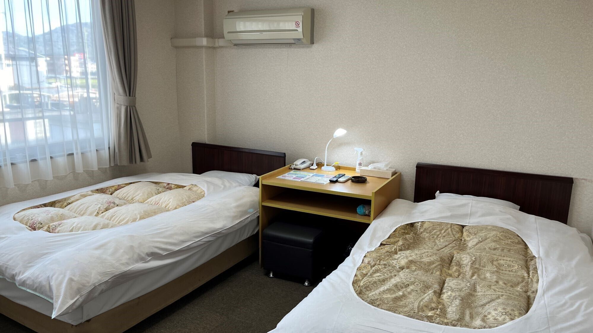 Een hotelkamer met twee bedden, een bureau met lamp, een telefoon en een klein plankje.