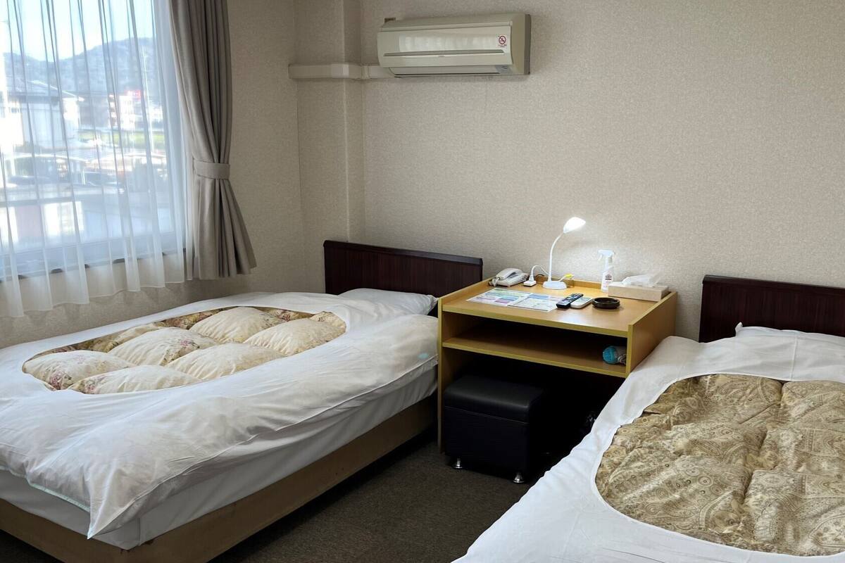 Une chambre d’hôtel avec deux lits, un bureau avec une lampe, un téléphone et une petite étagère.