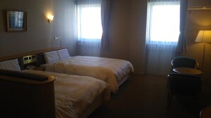 A hotel room with two beds, a bedside table with a lamp, a chair, and a window with curtains. - Hotel Hitachi Hills (Hitachi)