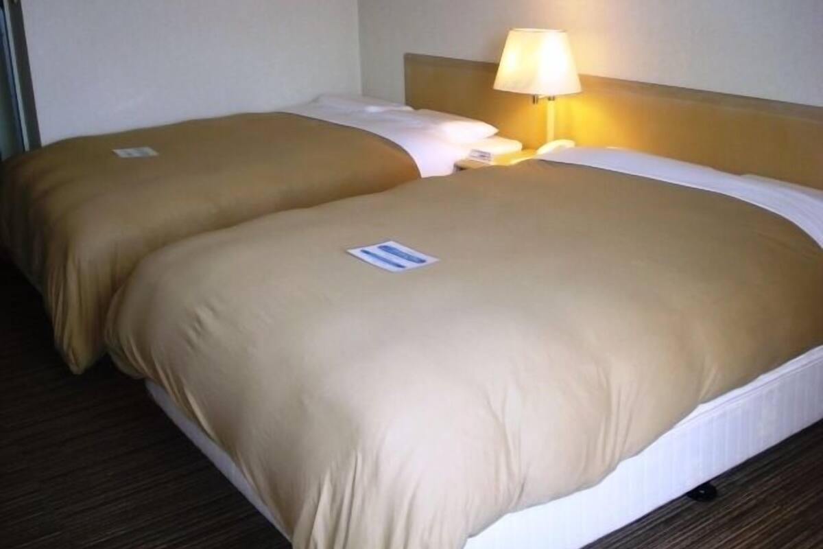 Uma cama de casal com roupa de cama bege e uma mesa de cabeceira com abajur.