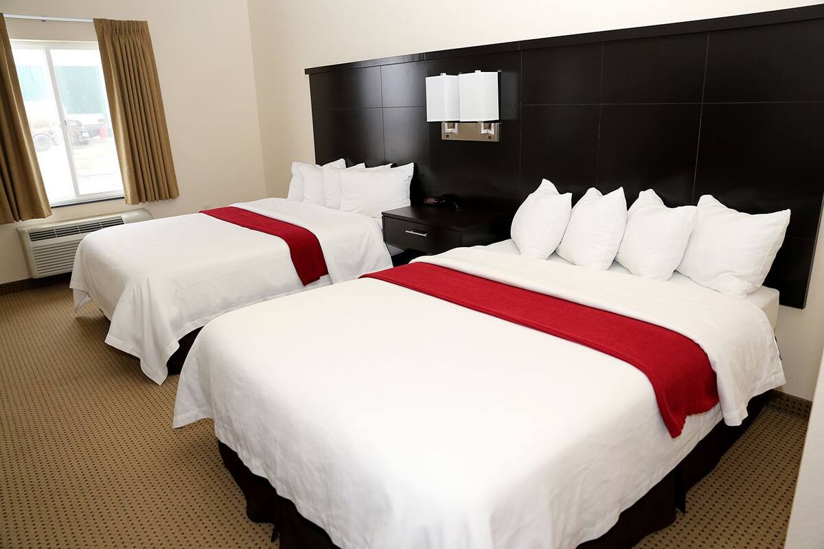 A hotel room with two beds, each with white bedding and red accents, a black headboard, and a window with curtains.