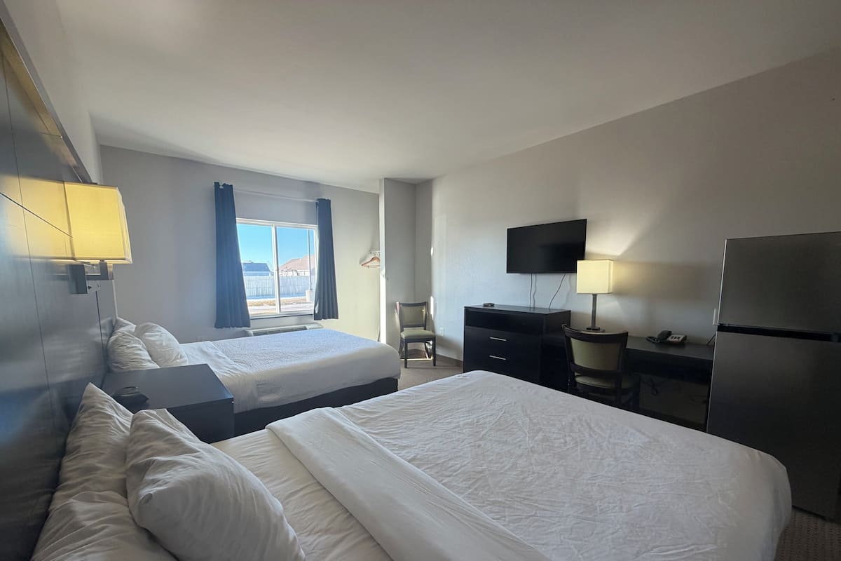 A hotel room with two beds, a desk, a chair, a TV, and a refrigerator.