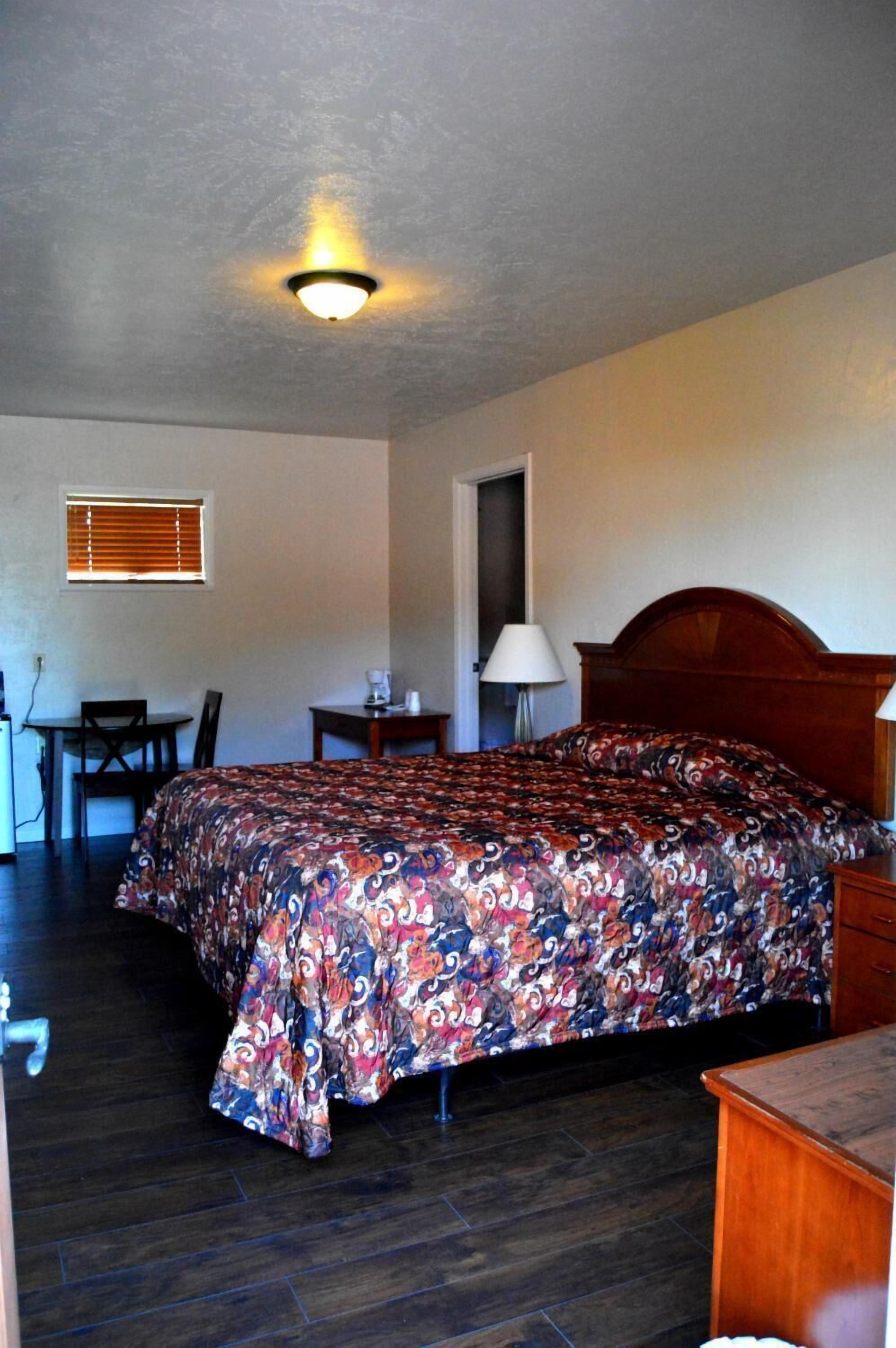 Une chambre d’hôtel équipée d’un lit, d’un bureau, d’une chaise, d’une lampe et d’un luminaire au plafond.