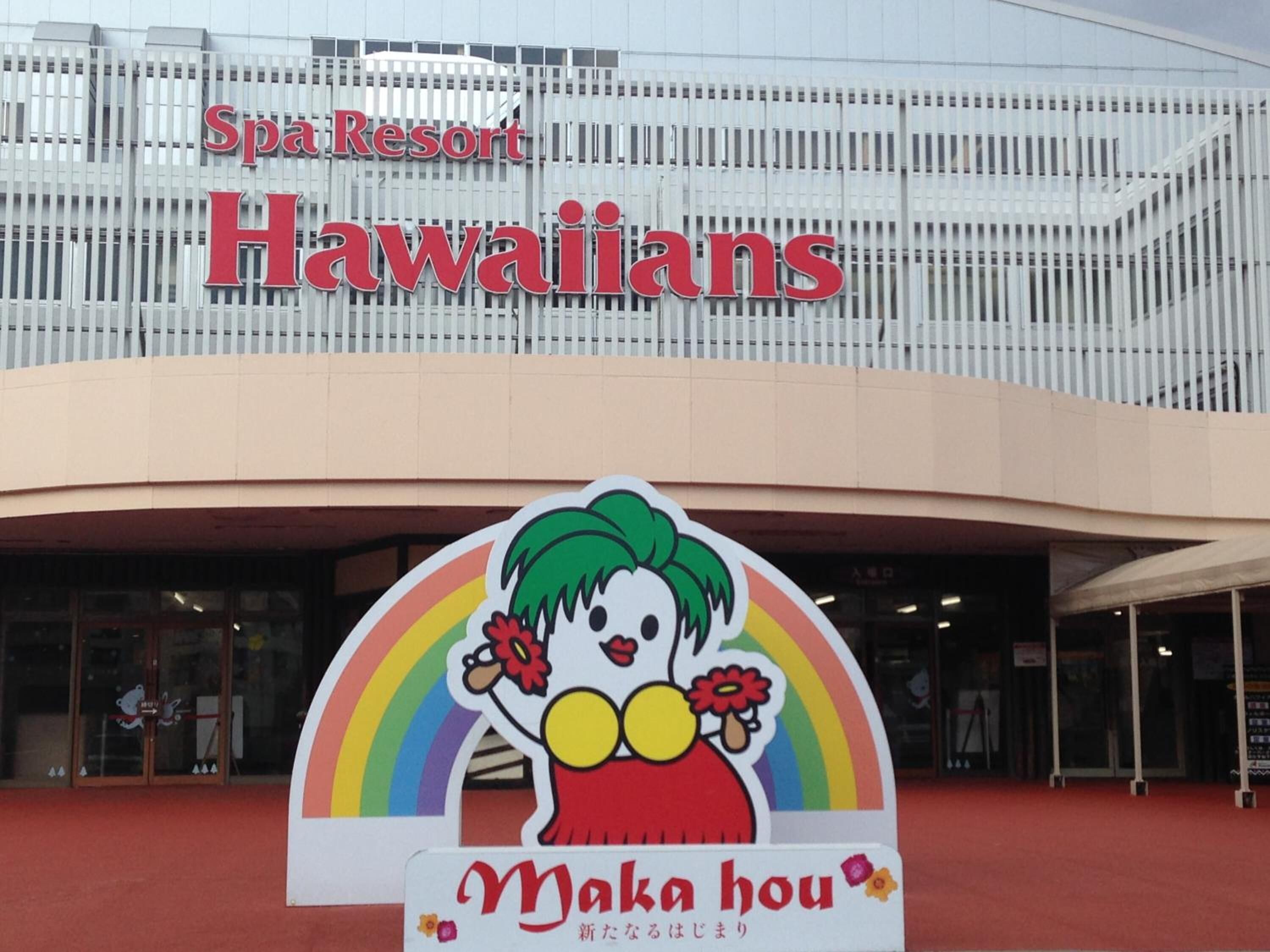 A building with a sign that reads 'Spa Resort Hawaiians' and a colorful mascot sign for 'Maka hou' in front.