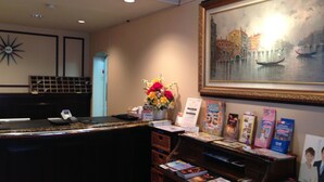 Un mostrador de recepción con un cuadro de un paisaje urbano, un florero con flores y una exhibición de revistas.